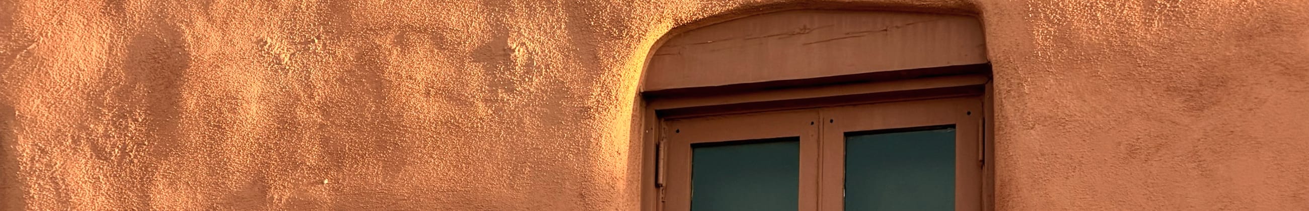 Warm afternoon light across a hand-troweled adobe wall and window
