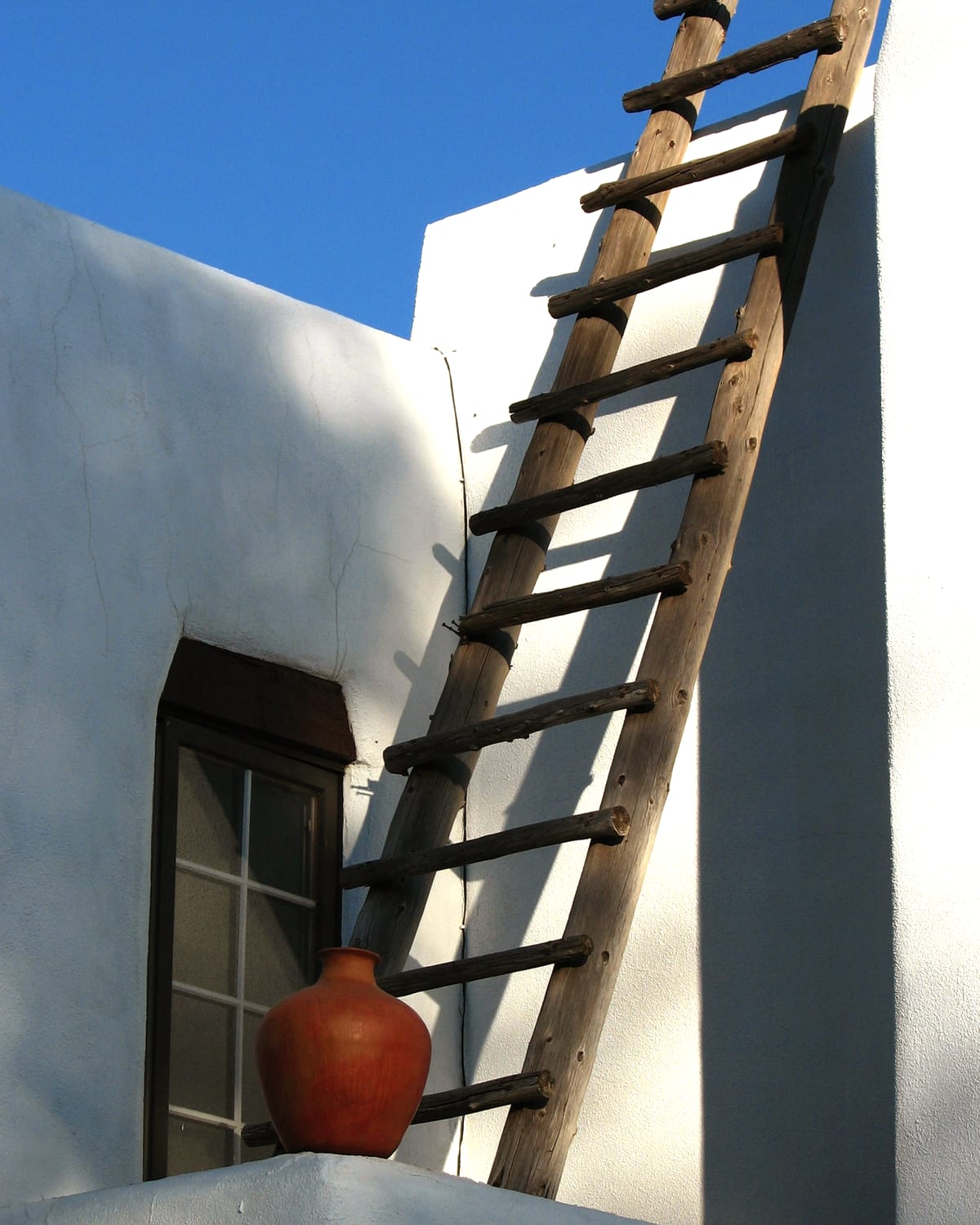 A wooden ladder leaning against a white adobe wall under a clear sky